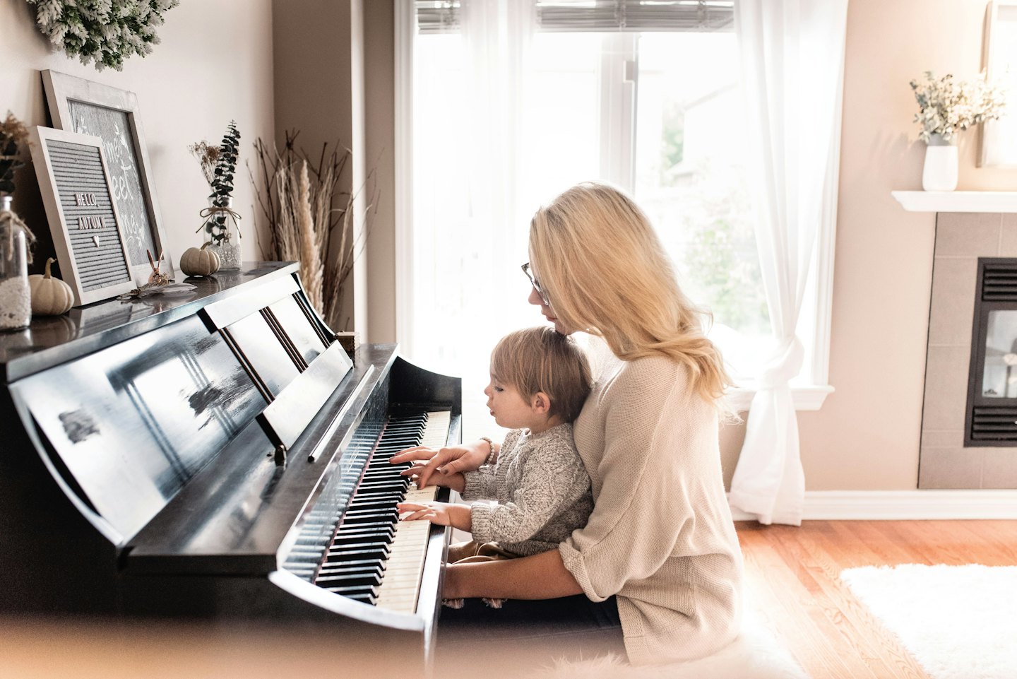 Vrouw leert kind piano spelen met pompoenen erop.